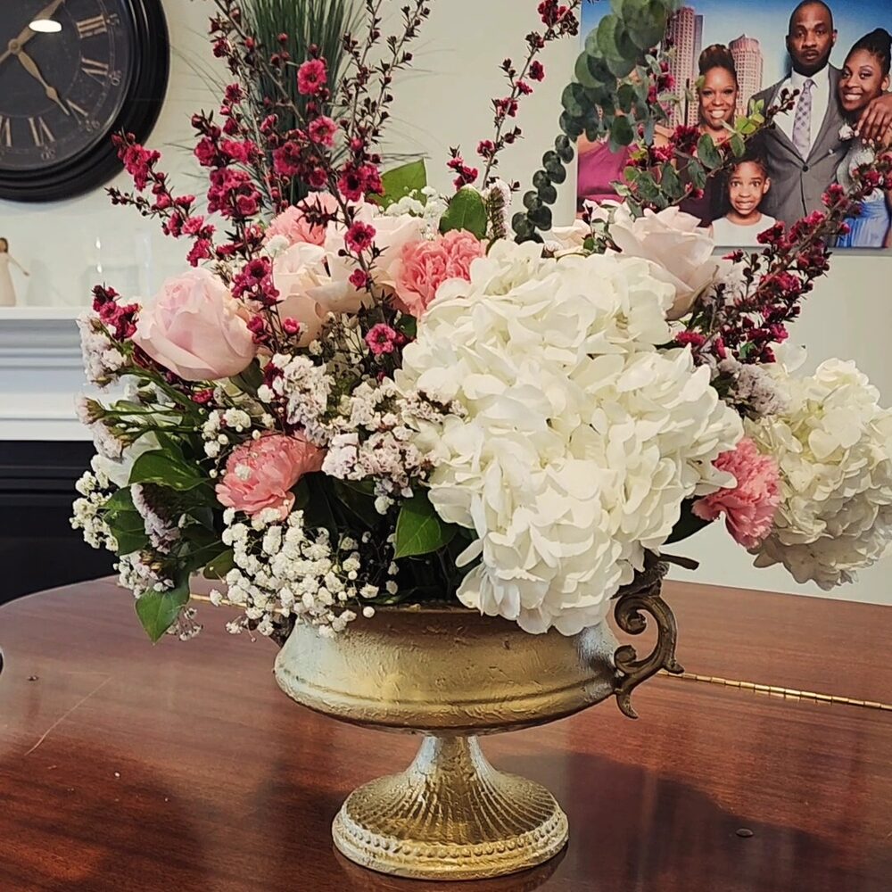 Gold vase with pink and white flower arrangement beside a family photo