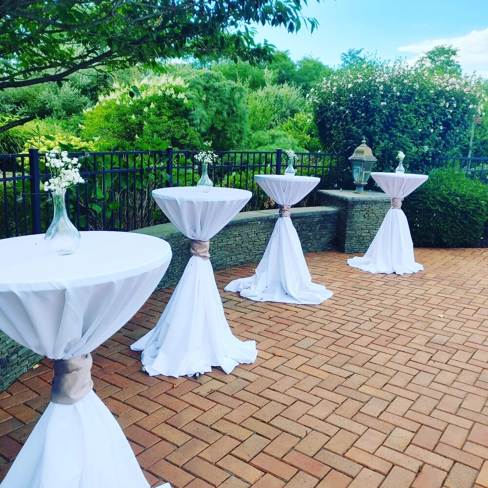 White cocktail tables arranged on a garden patio for an outdoor event