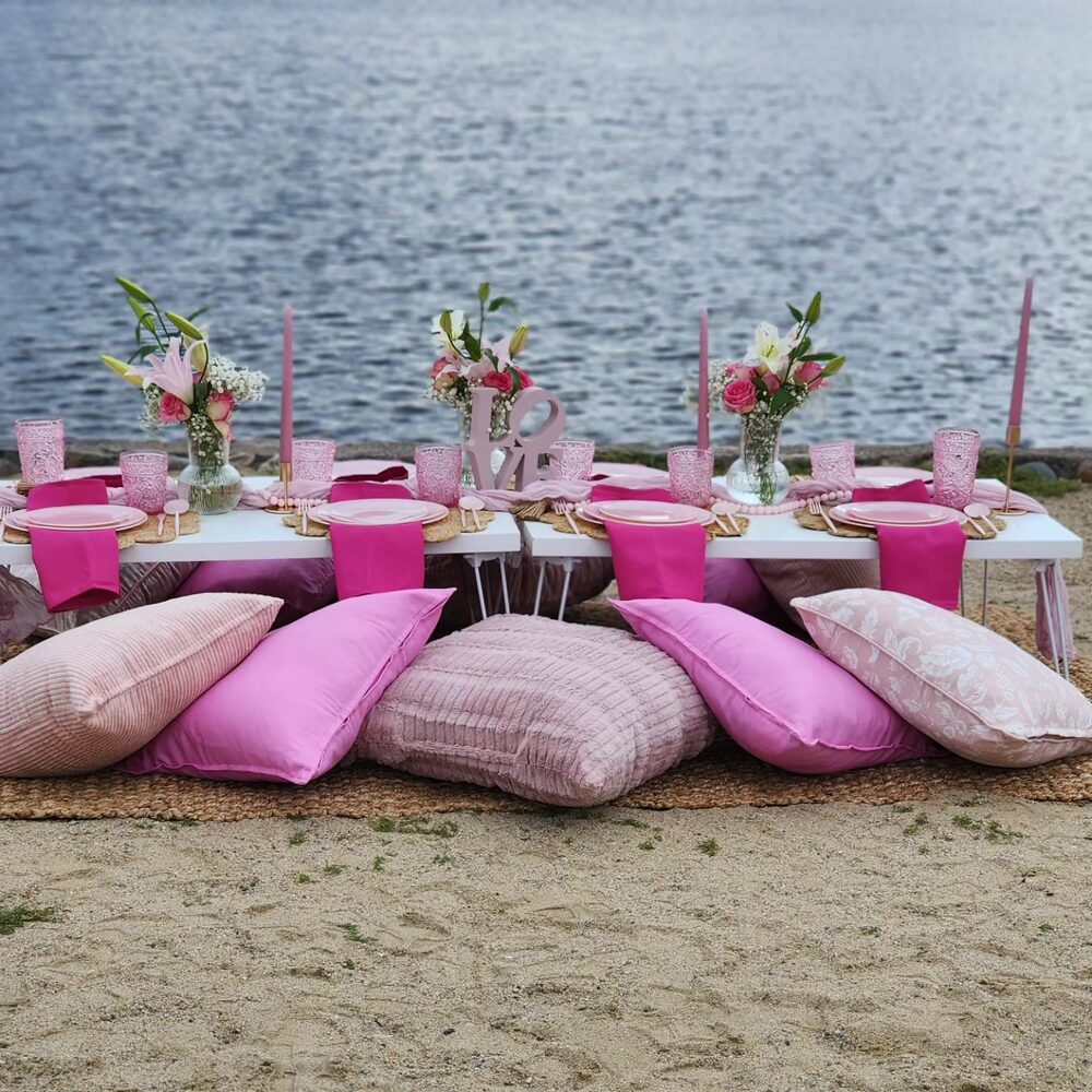 Pink beach picnic setup on the waterfront with pillows